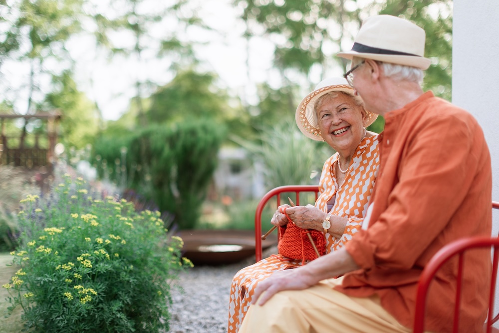 Senior woman sitting in the garden on the bench with her husband and knitting scarf at their assisted living communities